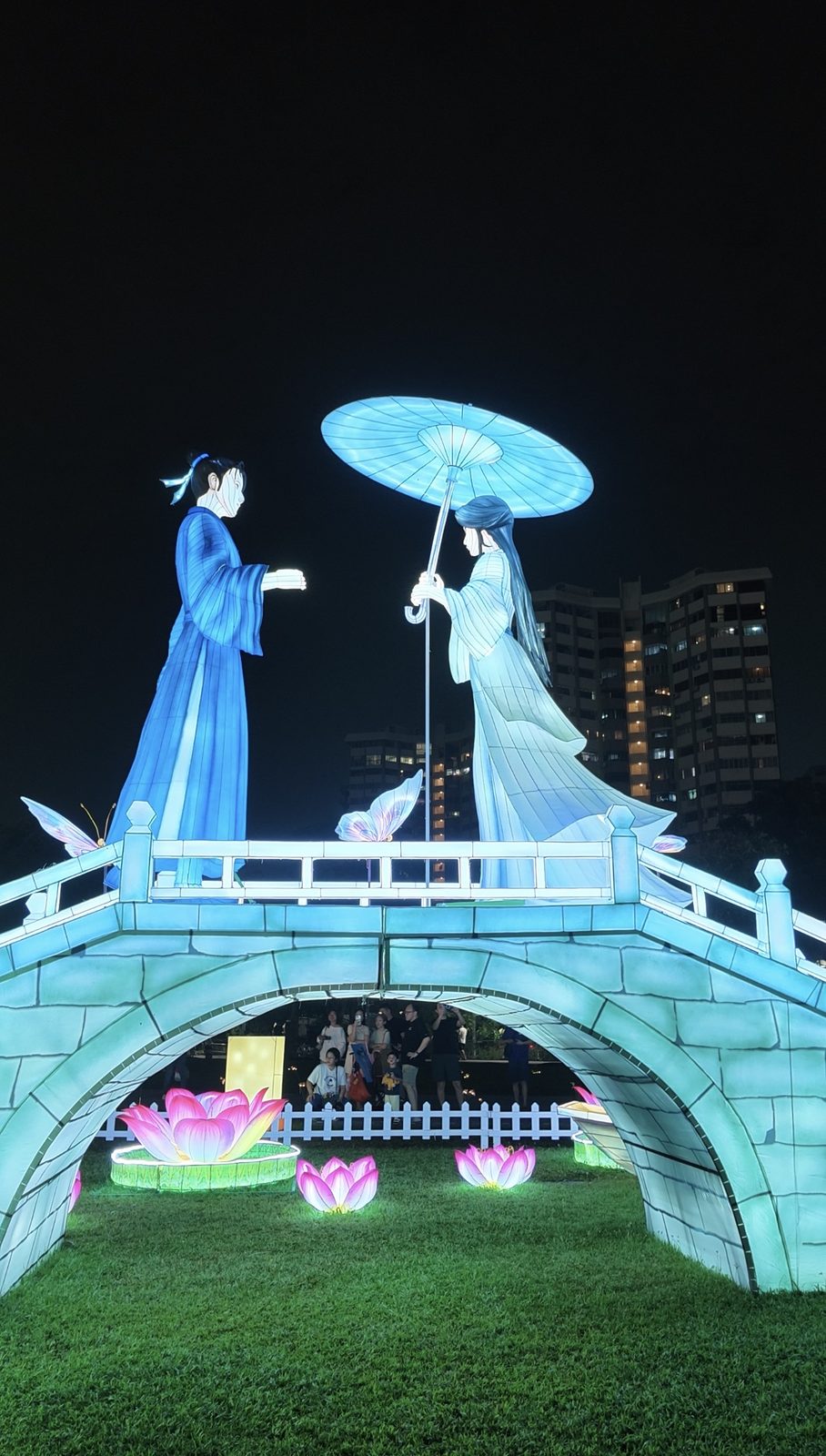 Two lantern figures meeting on a lit stone bridge, with lotus lanterns below