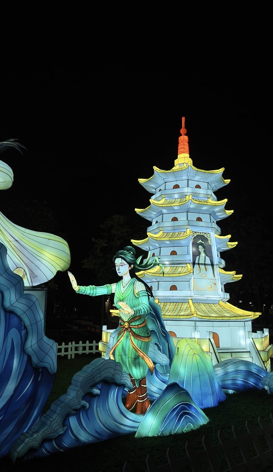 A lantern figure in green robes reaching towards a pagoda lantern, with a woman pictured in its window