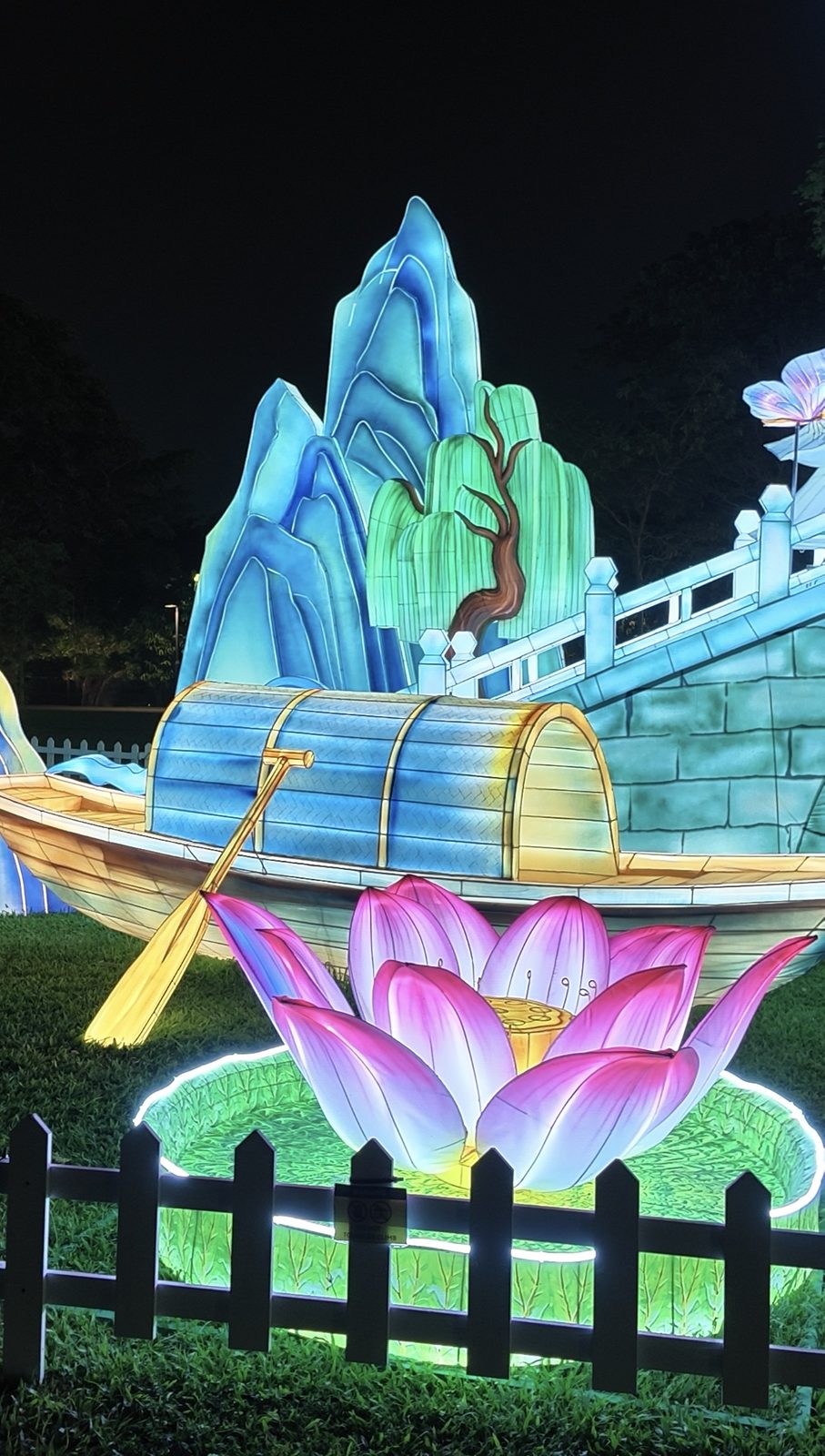 A lantern boat with an oar in front of mountain and willow lanterns
