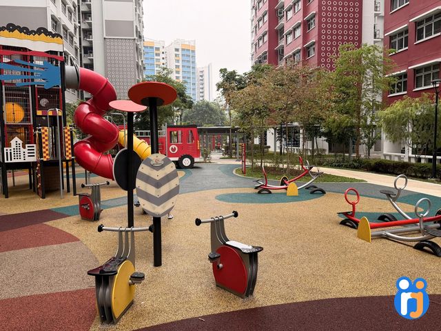 Spinner seats, a sound panel and four-seat seesaws on a colourful rubber floor, with the red spiral slide tower and the play fire engine behind.