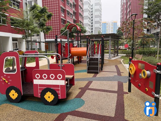 The toddler corner, with a small red play fire engine, a low play structure with an orange tunnel and a sensory panel with yellow wheels.