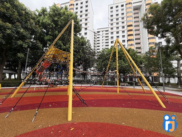 Two yellow-framed rope pyramids of different heights on a striped red and ochre rubber floor, with HDB blocks behind.