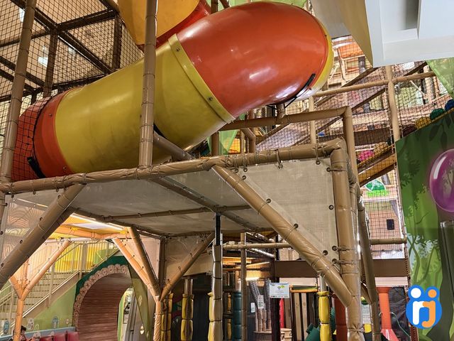 A wide orange-and-yellow tube slide curves down through the timber-framed play structure.