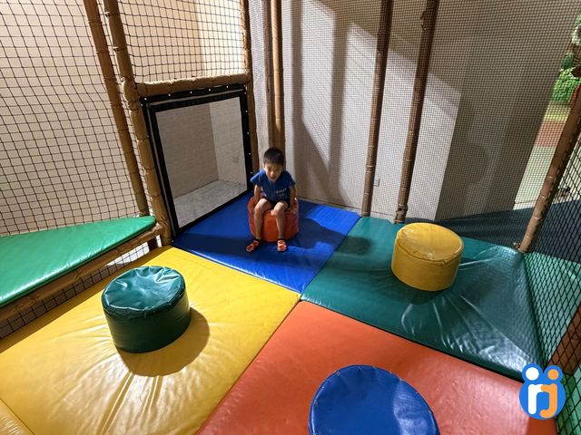 A netted soft-play room with padded mats and poufs for younger children, with a boy sitting inside.